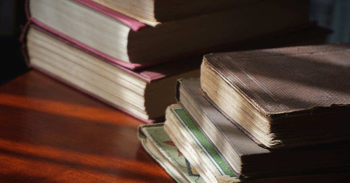 Pilha de livros de capa dura antigos sobre mesa de madeira, iluminada por luz lateral
