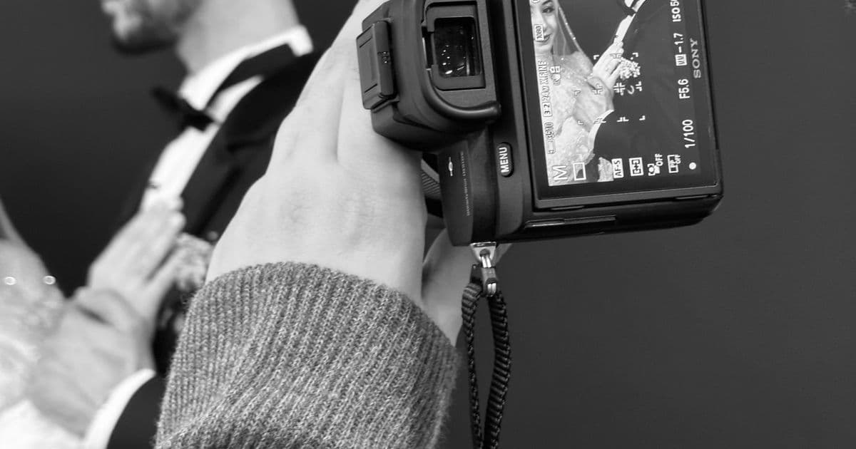 Fotógrafo segurando a câmera durante um casamento, com os noivos enquadrados na tela do equipamento